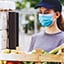 Two masked people interact over a crates of food at a farmer’s market