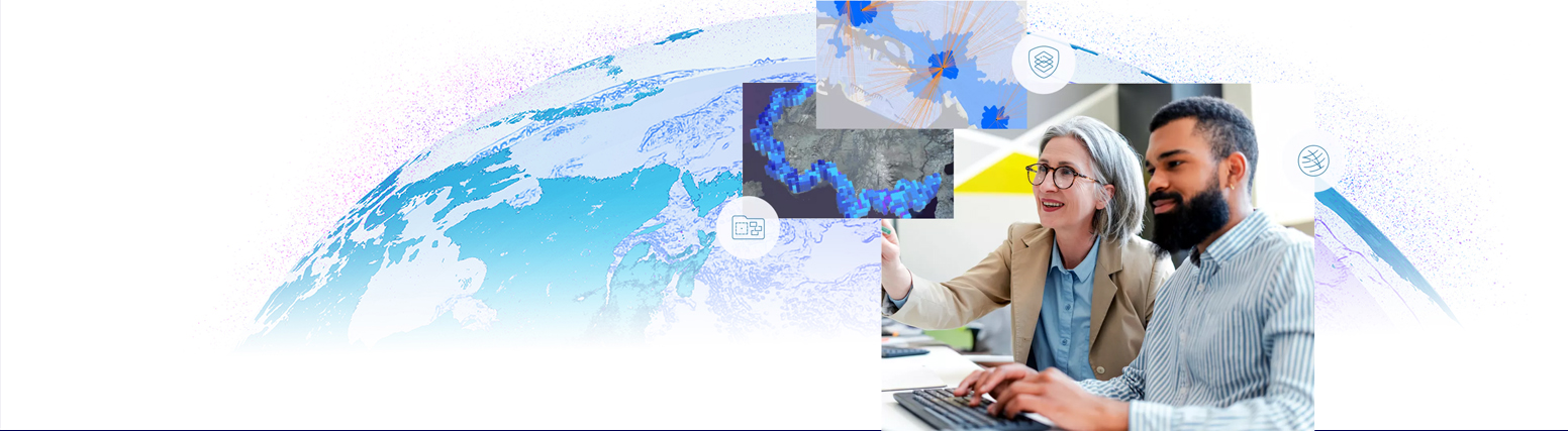 A woman gestures to a computer screen displaying digital maps and icons, while a man beside her observes