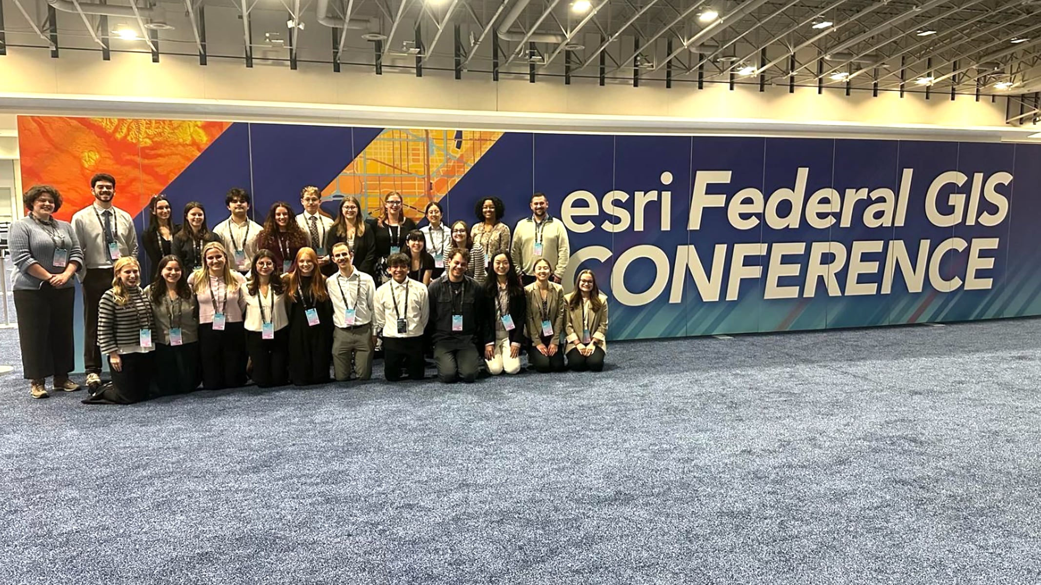 A group of people pose for a photo by a wall at the Esri Federal GIS Conference