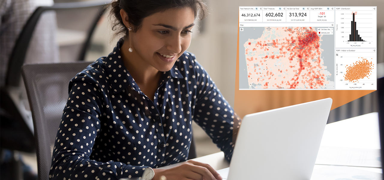 A person sitting in a classroom wearing a blue and white polka-dotted shirt smiling at a laptop monitor, which is displaying a map dashboard