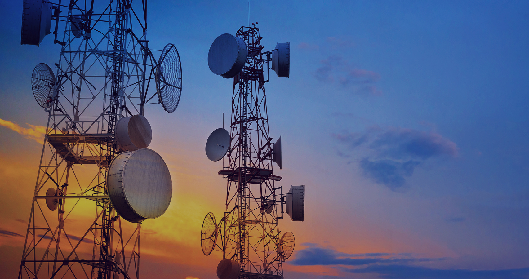 A photo of the top of a cellular base station against an orange and blue sky