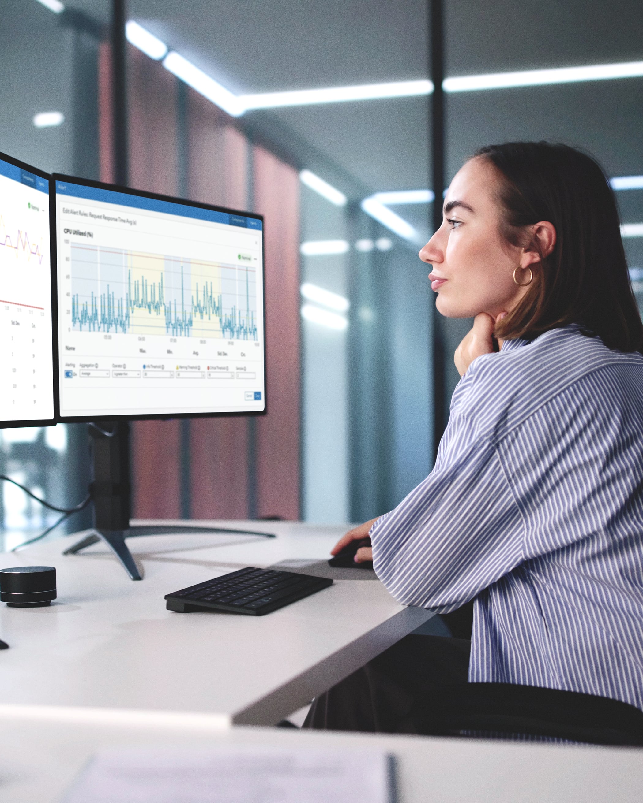 A person looking at two computer screens that display GIS dashboards that show system performance