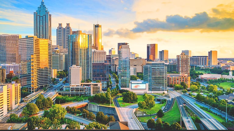 Aerial view of a sprawling modern city with spacious tree-filled parks under a calm sunrise sky