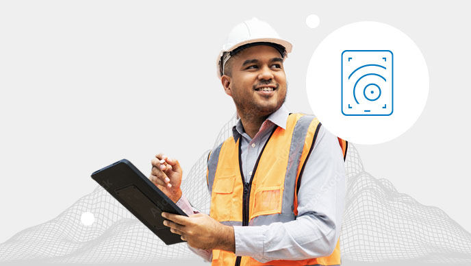 A man in an orange vest and white hard hat holding a tablet with an inset icon in a white circle