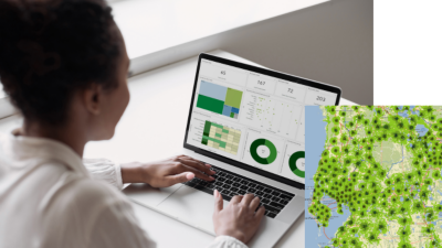 A business professional working on a laptop that displays a mapping dashboard interface, overlaid by a square map marked with many green marks